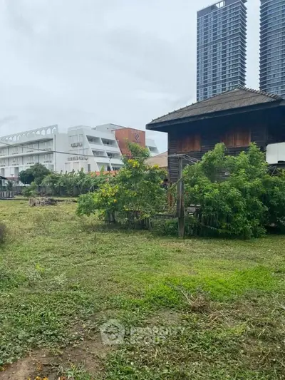 Charming rustic house with lush garden and modern high-rise backdrop, perfect blend of nature and urban living.