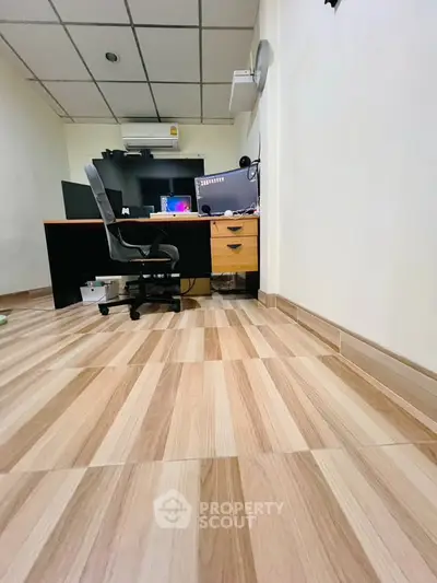 Modern home office with ergonomic chair and dual monitors on wooden flooring.
