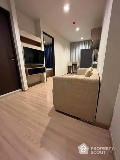 Elegant modern living room with sleek wooden flooring, cozy sofa, and a mounted TV, leading to a well-lit dining area with stylish curtains.