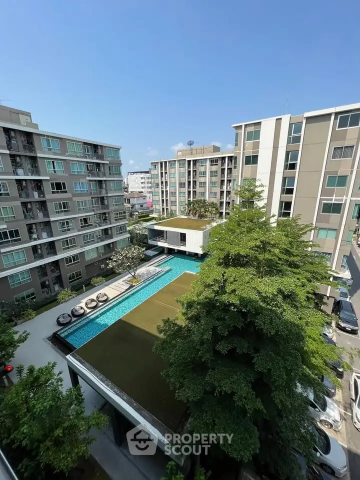 Modern apartment complex with pool and lush greenery under clear blue sky.