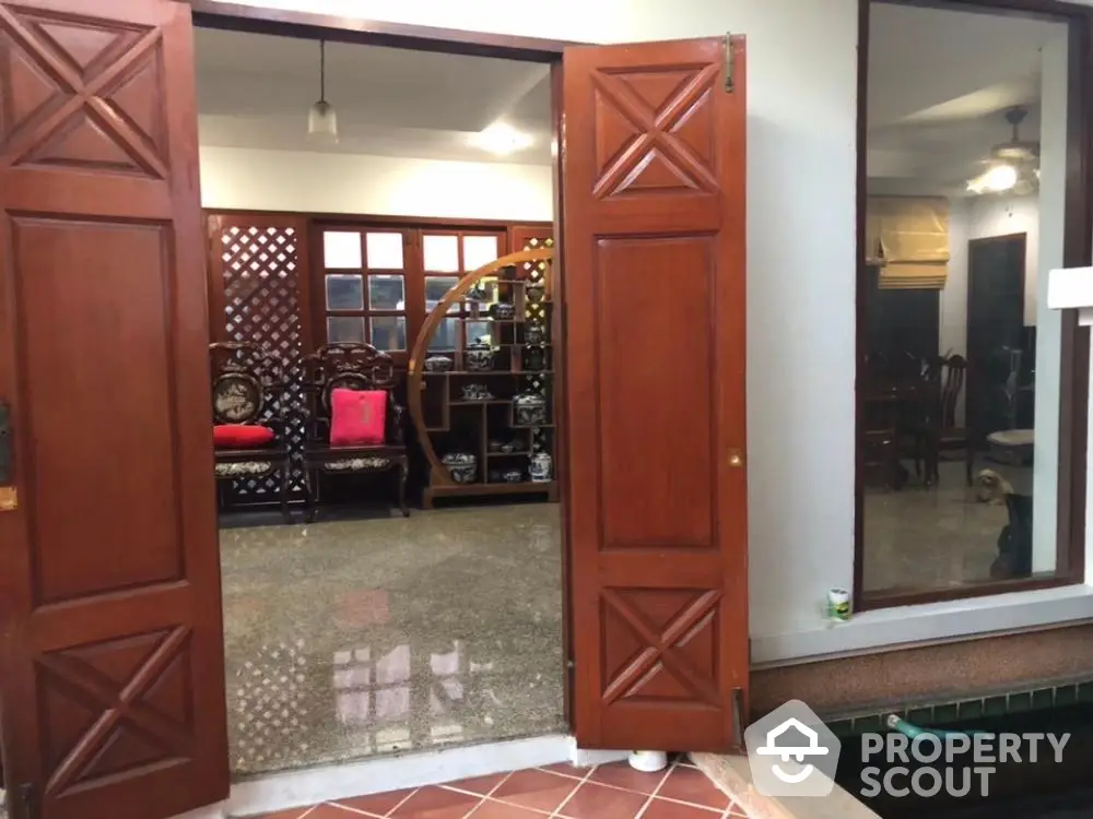 Elegant home entrance with open wooden doors leading to a spacious living area with traditional furniture and decorative partitions.