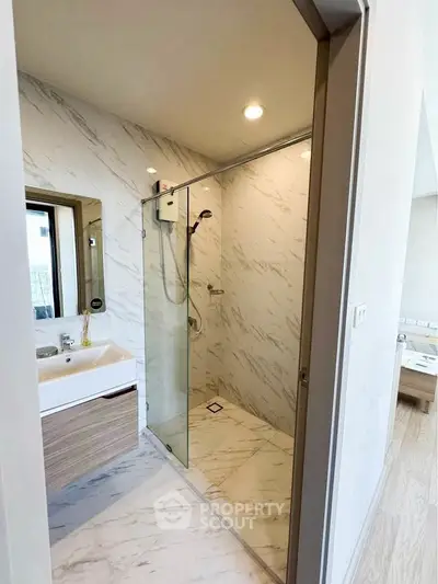 Modern bathroom with glass shower and marble tiles, sleek vanity and natural light.