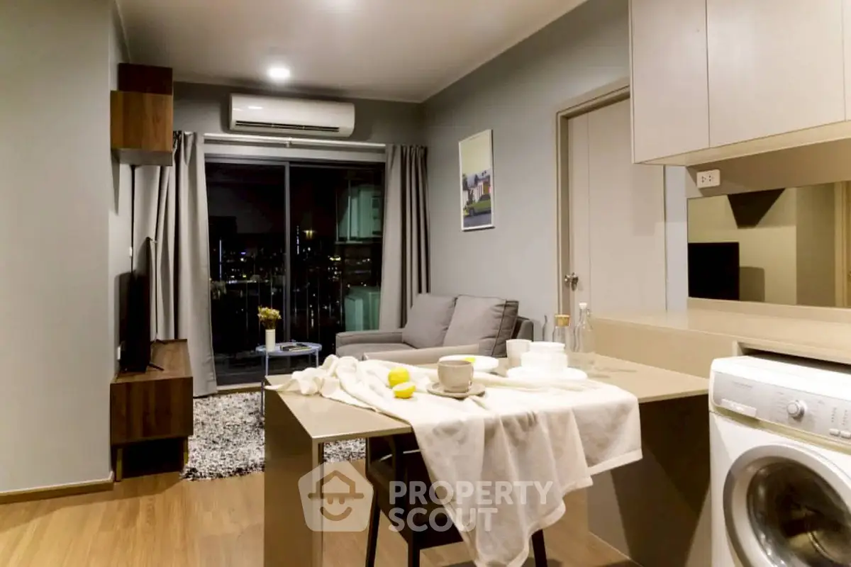 Modern living room with open kitchen and washing machine, featuring cozy seating and city view.
