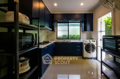 Modern kitchen with dark cabinets and washing machine, featuring sleek appliances and natural light.