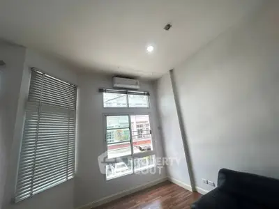Bright living room with large windows and air conditioning, featuring sleek wooden flooring and modern blinds.