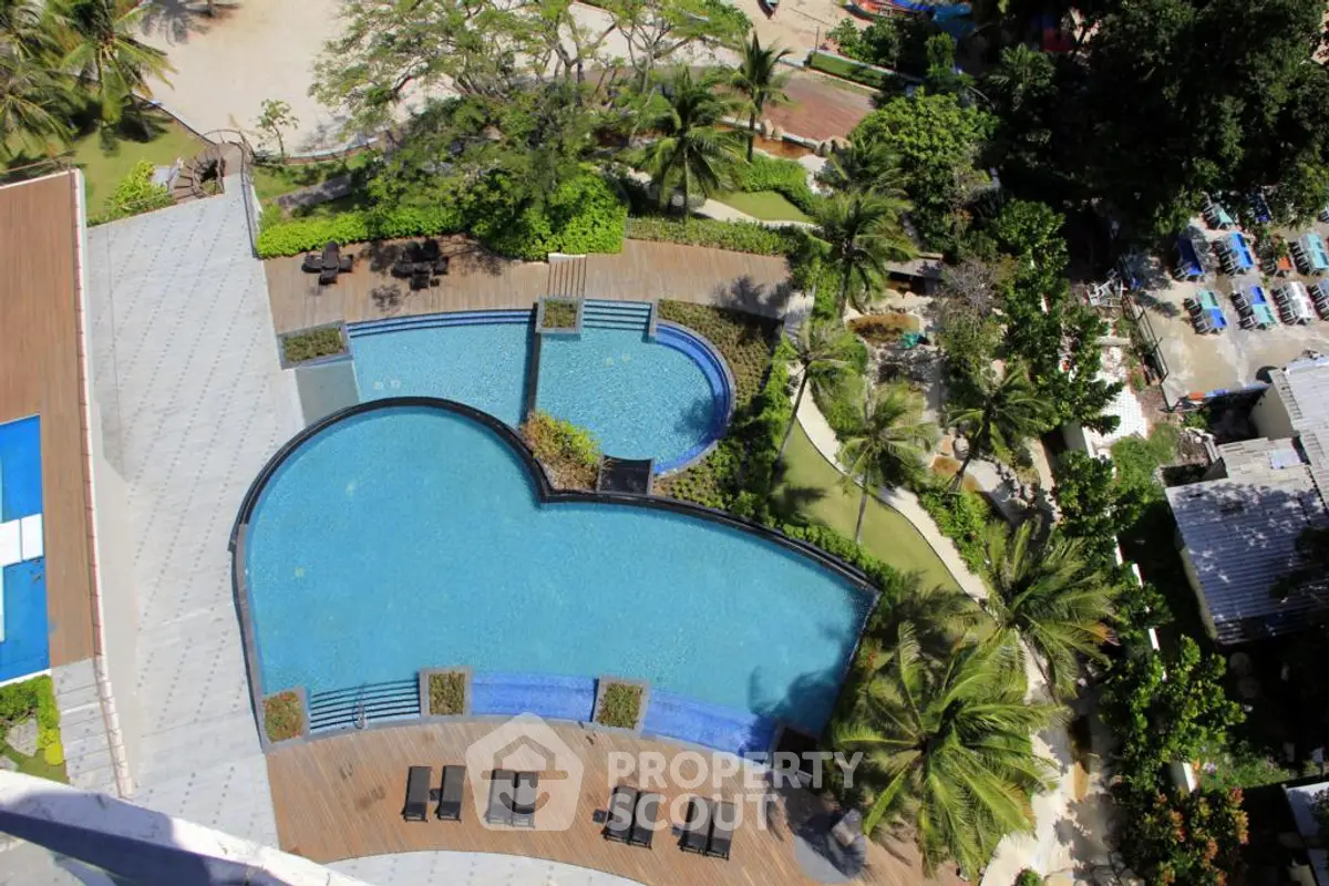 Stunning aerial view of a luxurious heart-shaped swimming pool surrounded by lush greenery and sun loungers.