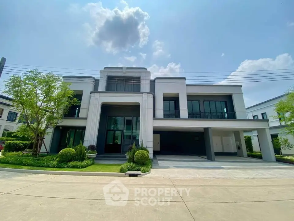 Luxurious modern house with spacious driveway and manicured garden under a clear blue sky.