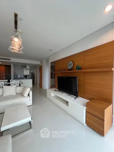 Modern living room with sleek design and open kitchen layout, featuring a large TV and stylish furniture.