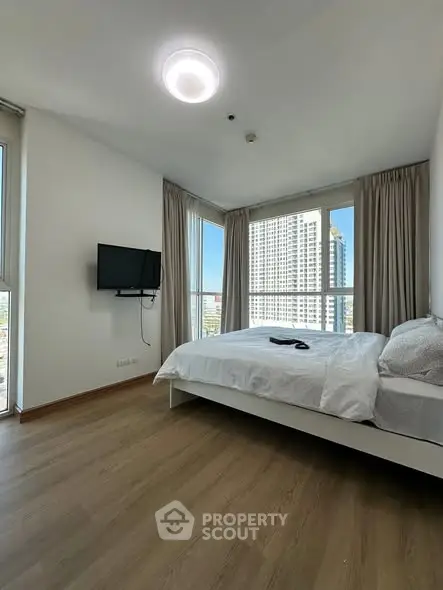 Modern bedroom with large windows and city view, featuring a wall-mounted TV and cozy bed.