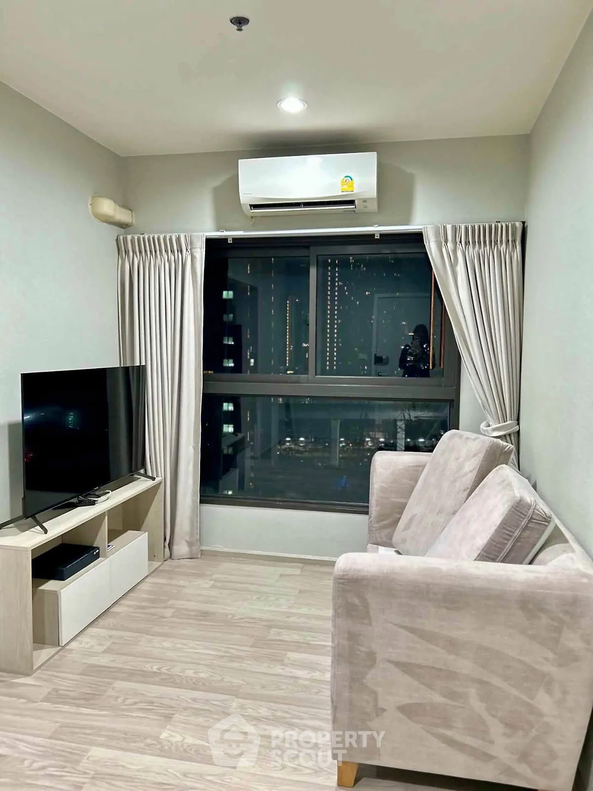 Modern living room with city view, featuring sleek furniture and air conditioning.