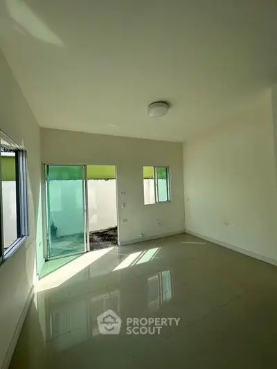 Bright empty room with large windows and sliding glass door leading to a small outdoor area.