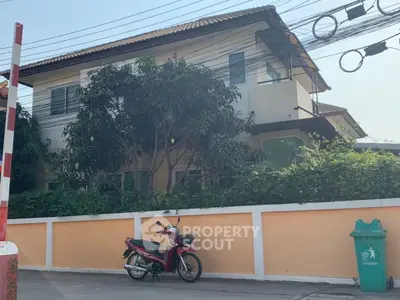 Charming two-story house with lush greenery and privacy wall, perfect for serene living.