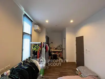 Spacious bedroom with wooden flooring and ample natural light, featuring a clothing rack and modern air conditioning.