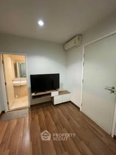 Modern living room with wooden flooring and wall-mounted TV, adjacent to a sleek bathroom.