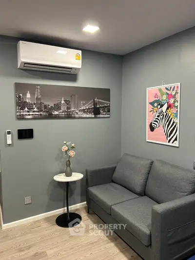 Modern living room with gray sofa, wall art, and air conditioning unit.
