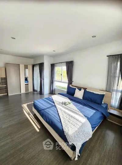 Spacious bedroom with modern decor and large windows offering natural light.