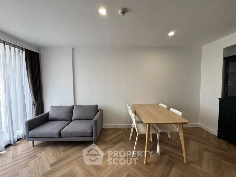 Modern living room with stylish gray sofa and wooden dining table, featuring elegant herringbone flooring.