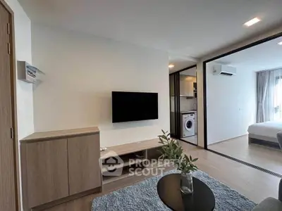 Modern living room with sleek TV setup and view into bedroom with washing machine.