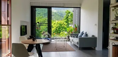 Modern living room with large windows offering stunning mountain views and lush greenery.