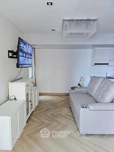 Modern living room with sleek sofa and wall-mounted TV, featuring elegant herringbone flooring.