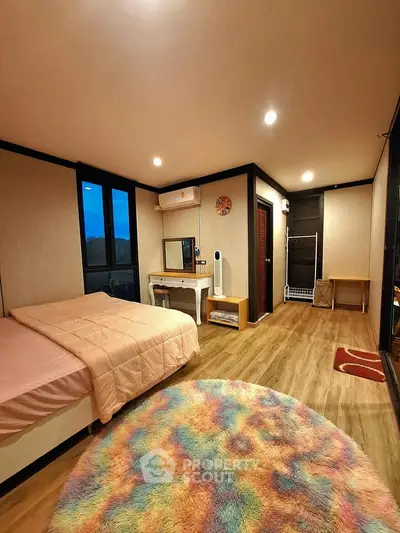 Cozy bedroom with modern decor, featuring a colorful rug and ample natural light.
