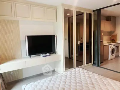 Modern bedroom with TV and mirrored closet, adjacent to kitchen with washing machine.