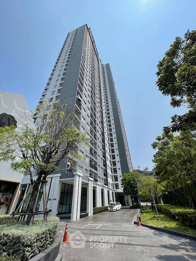 Modern high-rise residential building with lush greenery and clear blue sky.
