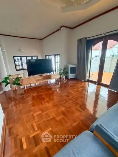 Spacious living room with polished wooden floors and large windows opening to a patio.