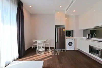 Modern kitchen with sleek appliances and dining area, featuring a washing machine and fridge.