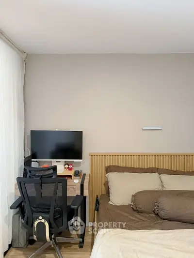 Modern bedroom with workspace featuring a desk, chair, and computer, alongside a cozy bed setup.