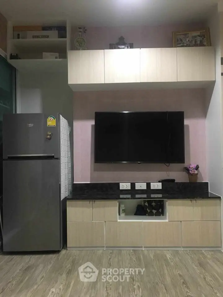 Modern living room with sleek TV setup and refrigerator, featuring stylish cabinetry.