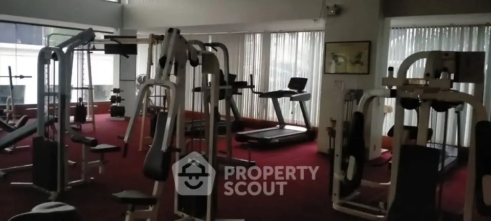 Spacious gym with modern fitness equipment and large windows for natural light.