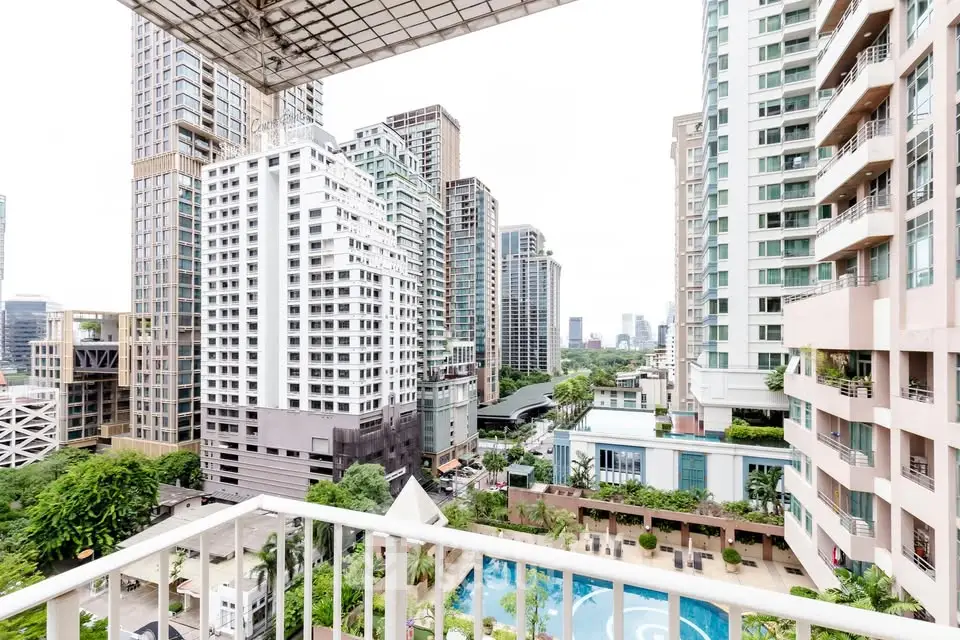 Stunning cityscape view from a high-rise balcony overlooking a pool and lush greenery.