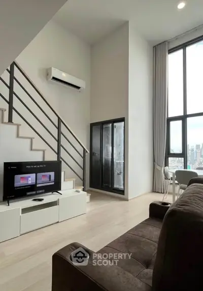 Modern loft apartment with high ceilings and city view, featuring a cozy living area and sleek staircase.