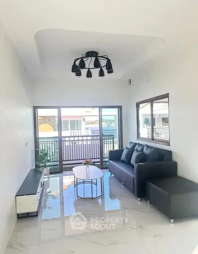 Modern living room with sleek black sofa and stylish chandelier, featuring large windows and balcony access.