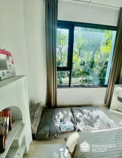 Cozy bedroom with large window and garden view, featuring a sewing machine and minimalist decor.