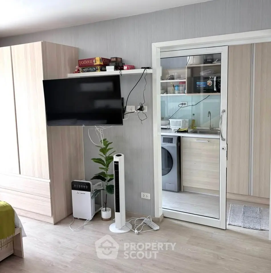 Modern apartment interior with TV, sliding glass door to kitchen, and laundry appliances.