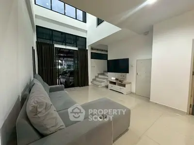 Spacious modern living room with high ceiling and large windows, featuring a cozy gray sofa and sleek entertainment unit.