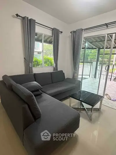 Modern living room with sleek gray sofa and glass coffee table, overlooking a spacious balcony.