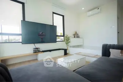 Modern living room with sleek furniture and large wall-mounted TV, featuring bright natural light and minimalist decor.