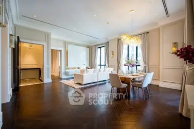 Luxurious living room with elegant dining area and chandelier, featuring hardwood floors and large windows.