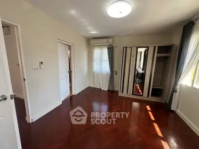 Spacious bedroom with wooden flooring and ample natural light, featuring a built-in wardrobe and air conditioning.