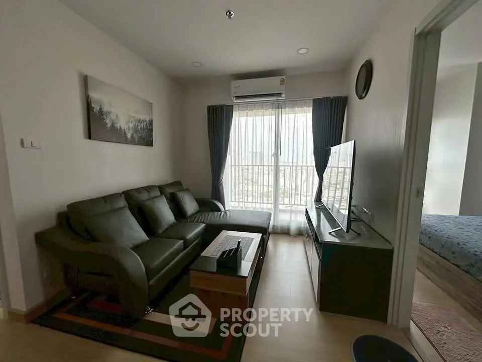 Modern living room with leather sofa and large TV, featuring natural light from a window with curtains.