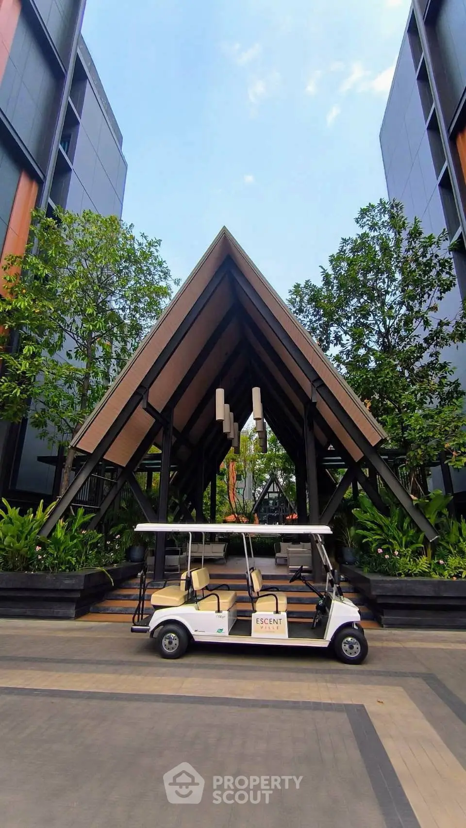 Modern building entrance with unique architectural design and lush greenery, featuring a golf cart for convenient transport.