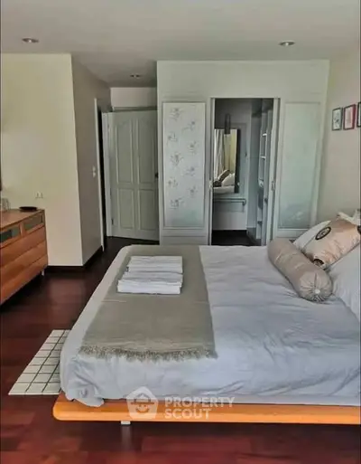 Spacious bedroom with modern decor and wooden flooring, featuring a cozy bed and ample natural light.