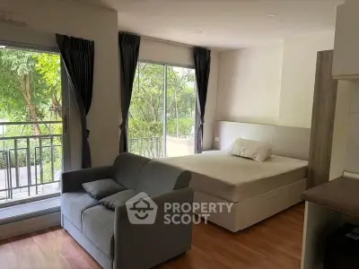 Cozy studio apartment with large windows and balcony overlooking lush greenery.