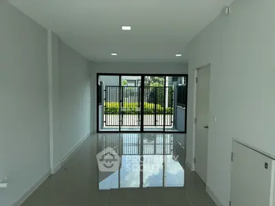 Modern empty room with glossy tiled floor and large sliding glass doors leading to a garden view.