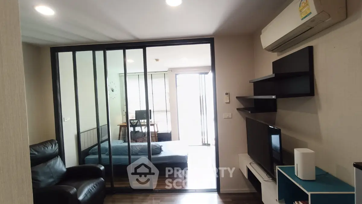 Modern living room with sliding glass doors leading to a cozy bedroom, featuring sleek furniture and air conditioning.