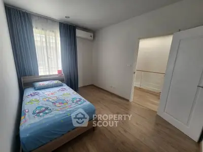 Cozy bedroom with wooden flooring and playful bedding, featuring natural light and modern air conditioning.