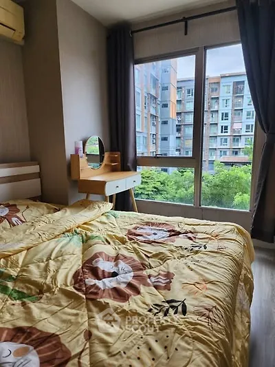 Cozy bedroom with large window offering a view of modern apartment buildings.